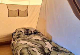 Innenaufnahme eines Safarizelts mit einem Einzelbett und blattgemusteter Bettwäsche in den Niederlanden.