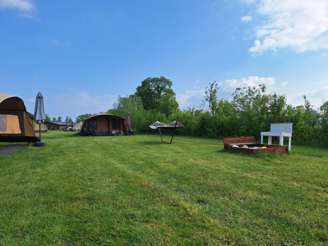 Safari tent at CharmeCamping De Regge-Vallei in the Netherlands, with grassy field, hammock, and sandbox.