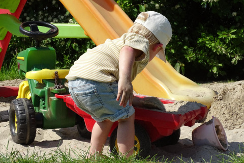 Niño pequeño jugando con arena, tractor de juguete y tobogán en CharmeCamping De Regge-Vallei, Países Bajos.