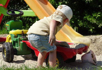 Niño pequeño jugando con arena, tractor de juguete y tobogán en CharmeCamping De Regge-Vallei, Países Bajos.