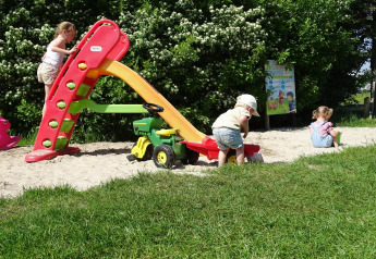 Niños juegan en un parque con tobogán y arena cerca de la tienda safari en CharmeCamping De Regge-Vallei.