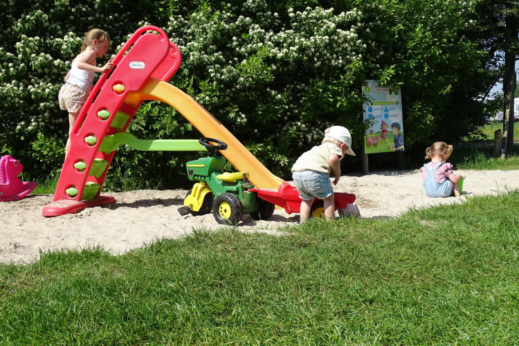 Children playing on a playground with a slide and sand at the Safari tent at CharmeCamping De Regge-Vallei.
