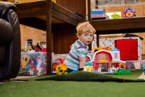Niño pequeño juega con juguetes en el suelo de una tienda safari, rodeado de cajas con bloques de colores.