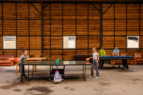 Kinderen spelen tafeltennis en biljart in een gemeenschappelijke ruimte met houten muren op een safari tentenkamp.