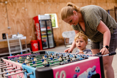 Mother and child play foosball together inside a safari tent lounge area with a fridge in the background.
