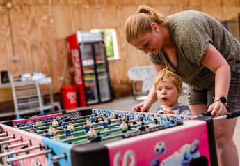 Madre e hijo juegan juntos futbolín en el área común de una tienda safari con una nevera de fondo.