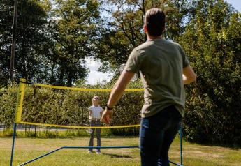 Twee mensen spelen badminton buiten bij een glamping accommodatie tussen de bomen en het gras.