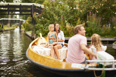 Familia disfruta de un paseo en bote por un canal pintoresco rodeado de vegetación y puentes pequeños.