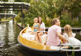 Familia disfruta de un paseo en bote por un canal pintoresco rodeado de vegetación y puentes pequeños.