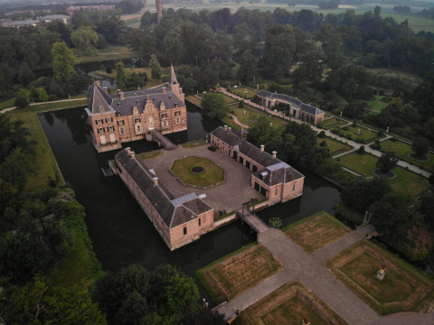 Vista aérea de un castillo rodeado de agua y jardines, tomada desde un alojamiento de glamping.