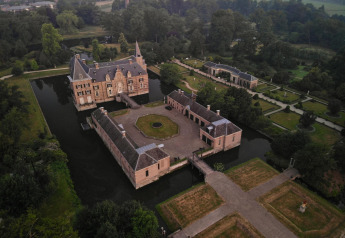 Vista aérea de un castillo rodeado de agua y jardines, tomada desde un alojamiento de glamping.
