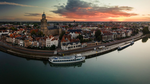 Panoramisch uitzicht bij zonsondergang over een Nederlandse stad met rivier, vanaf een glampinglocatie.
