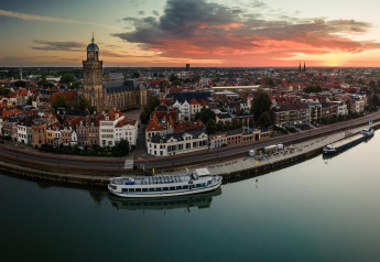 Panoramisch uitzicht bij zonsondergang over een Nederlandse stad met rivier, vanaf een glampinglocatie.