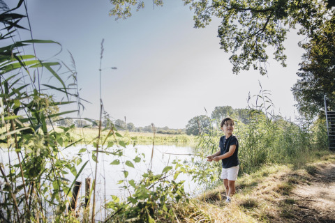 Kind vist bij een rivier naast safaritent bij CharmeCamping De Regge-Vallei in Nederland op zonnige dag.