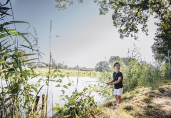 Kind vist bij een rivier naast safaritent bij CharmeCamping De Regge-Vallei in Nederland op zonnige dag.