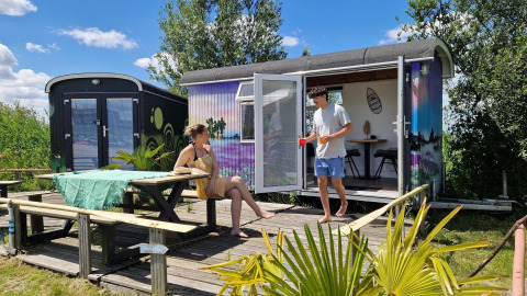 Dos personas se relajan frente a una colorida tiny house llamada Tiny wagon en Marina Parcs Almere, Países Bajos.