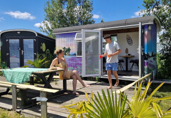 Dos personas se relajan frente a una colorida tiny house llamada Tiny wagon en Marina Parcs Almere, Países Bajos.