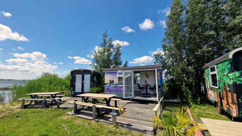 Buitenaanzicht van Tiny Wagon bij Marina Parcs Almere, Nederland, met picknicktafels en uitzicht op het meer.