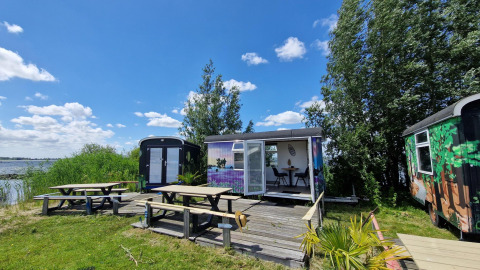 Vista exterior del Tiny Wagon en Marina Parcs Almere, Países Bajos, con bancos de picnic y vista al lago.