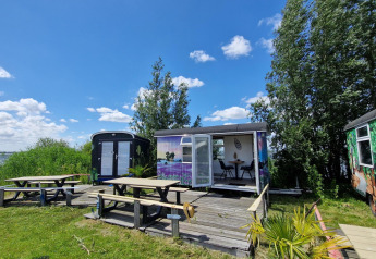 Vista exterior del Tiny Wagon en Marina Parcs Almere, Países Bajos, con bancos de picnic y vista al lago.