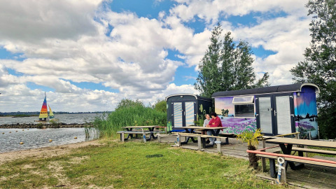 Twee mensen zitten aan een picknicktafel bij de Tiny Wagon van Marina Parcs Almere, Nederland, aan het meer.