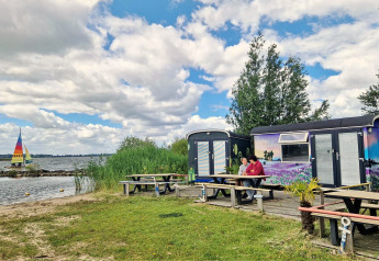 Due persone sedute a un tavolo da picnic davanti Tiny Wagon a Marina Parcs Almere, Paesi Bassi, vicino al lago.