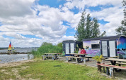Dos personas sentadas en una mesa de picnic frente al Tiny Wagon en Marina Parcs Almere junto al lago.