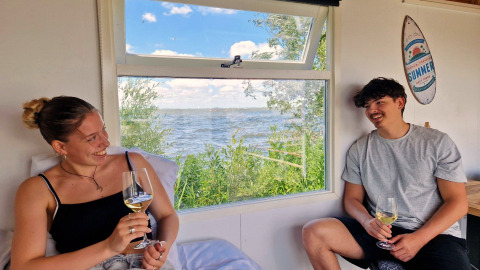 Twee jongeren genieten van wijn in de Tiny wagon bij Marina Parcs Almere, Nederland, met uitzicht op water.