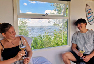 Twee jongeren genieten van wijn in de Tiny wagon bij Marina Parcs Almere, Nederland, met uitzicht op water.
