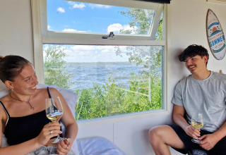 Due giovani adulti si godono il vino nella Tiny wagon al Marina Parcs Almere, Paesi Bassi, vista lago.
