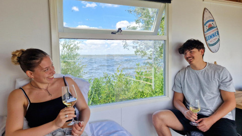 Deux jeunes adultes savourent du vin dans un Tiny wagon à Marina Parcs Almere, Pays-Bas, face à l’eau.