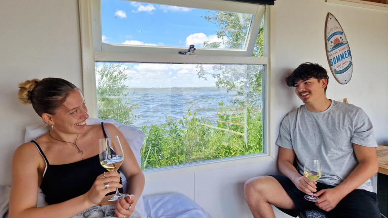 Dos jóvenes disfrutan vino en una Tiny wagon de Marina Parcs Almere, Países Bajos, con vista al agua.