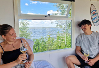 Due giovani adulti si godono il vino nella Tiny wagon al Marina Parcs Almere, Paesi Bassi, vista lago.
