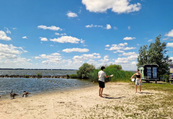 Due persone giocano sulla spiaggia vicino a una tiny wagon al Marina Parcs Almere, Paesi Bassi, sotto il sole.