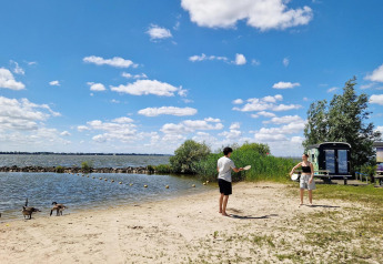 Zwei Menschen spielen am Strand neben dem Tiny Wagon im Marina Parcs Almere, Niederlande, bei Sonnenschein.
