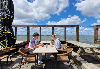 To personer sidder udenfor ved et bord med udsigt over vandet på Marina Parcs Almere i Holland.