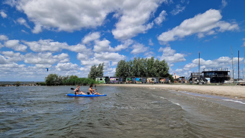Dos personas reman en kayak frente a Tiny Wagon en Marina Parcs Almere, Países Bajos, en un día soleado.
