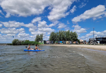 Dos personas reman en kayak frente a Tiny Wagon en Marina Parcs Almere, Países Bajos, en un día soleado.