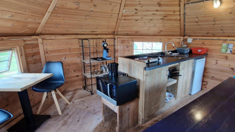 Pequeña cocina en Tiny Wagon con paredes de madera, mesa, sillas y electrodomésticos en Marina Parcs Almere.