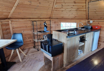 Pequeña cocina en Tiny Wagon con paredes de madera, mesa, sillas y electrodomésticos en Marina Parcs Almere.