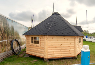 Klein houten huisje Tiny Wagon met zwart dak bij Marina Parcs Almere in Nederland, naast boten.