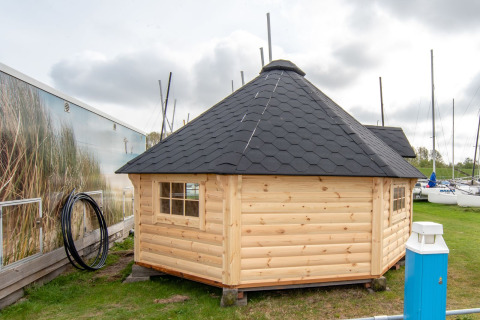 Pequeña casa de madera, Tiny Wagon, con techo negro en Marina Parcs Almere, Países Bajos, junto a barcos.
