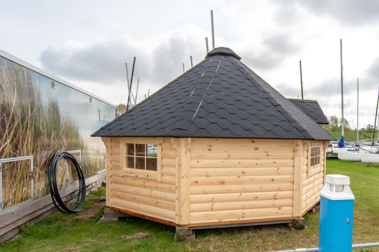 Pequeña casa de madera, Tiny Wagon, con techo negro en Marina Parcs Almere, Países Bajos, junto a barcos.