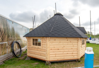Pequeña casa de madera, Tiny Wagon, con techo negro en Marina Parcs Almere, Países Bajos, junto a barcos.
