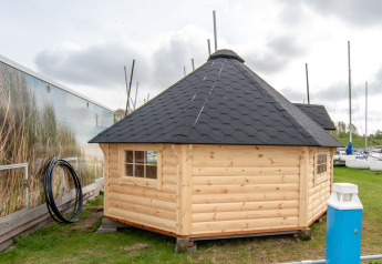 Piccola casa in legno Tiny Wagon con tetto nero presso Marina Parcs Almere nei Paesi Bassi, vicino a barche.