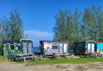 Tre farverige tiny houses ved søbredden med borde foran, fotograferet ved Tiny wagon, Marina Parcs Almere.