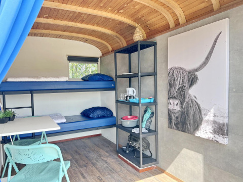 Interior del Tiny Wagon en Marina Parcs Almere con literas, estanterías y un gran cuadro de vaca