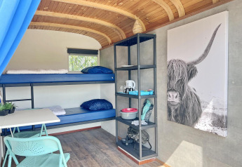 Interior del Tiny Wagon en Marina Parcs Almere con literas, estanterías y un gran cuadro de vaca