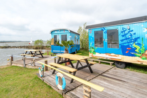 Casas pequeñas coloridas junto al agua, Tiny wagon en Marina Parcs Almere, Países Bajos, con mesas afuera.