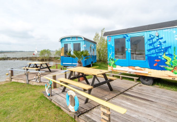 Casas pequeñas coloridas junto al agua, Tiny wagon en Marina Parcs Almere, Países Bajos, con mesas afuera.